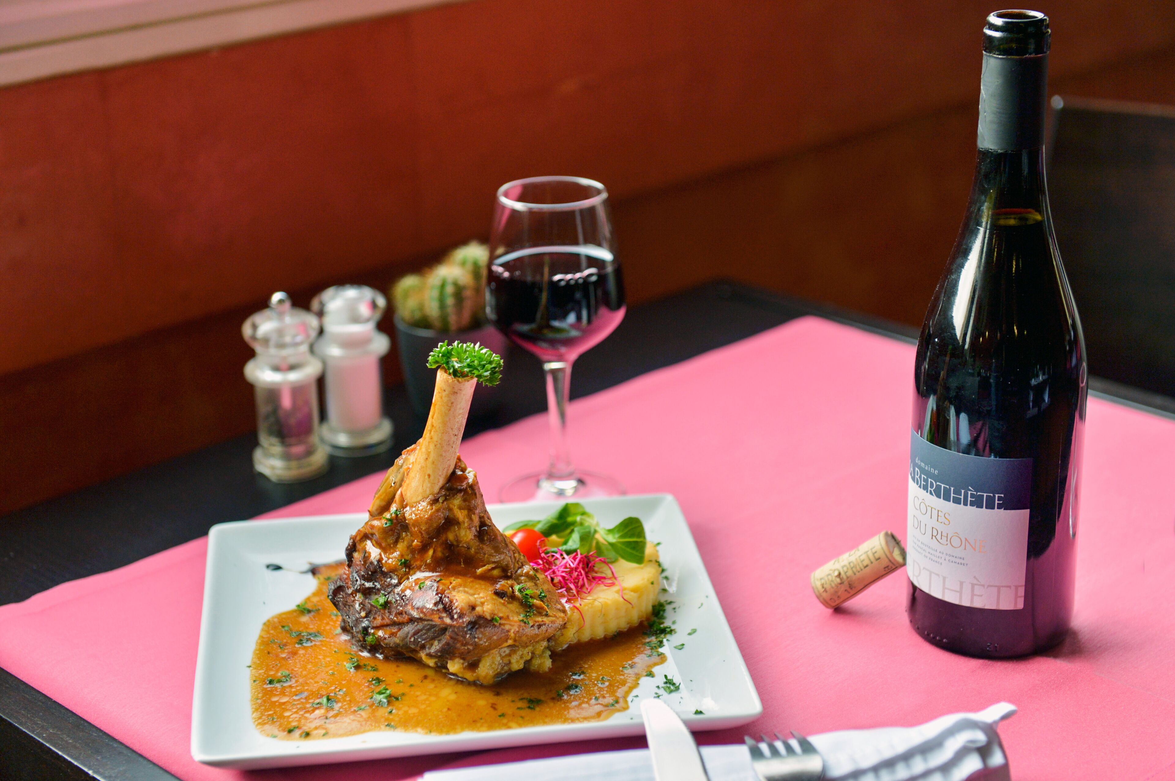 Un plato de comida con una botella de vino y una copa de vino tinto sobre un mantel rosa.