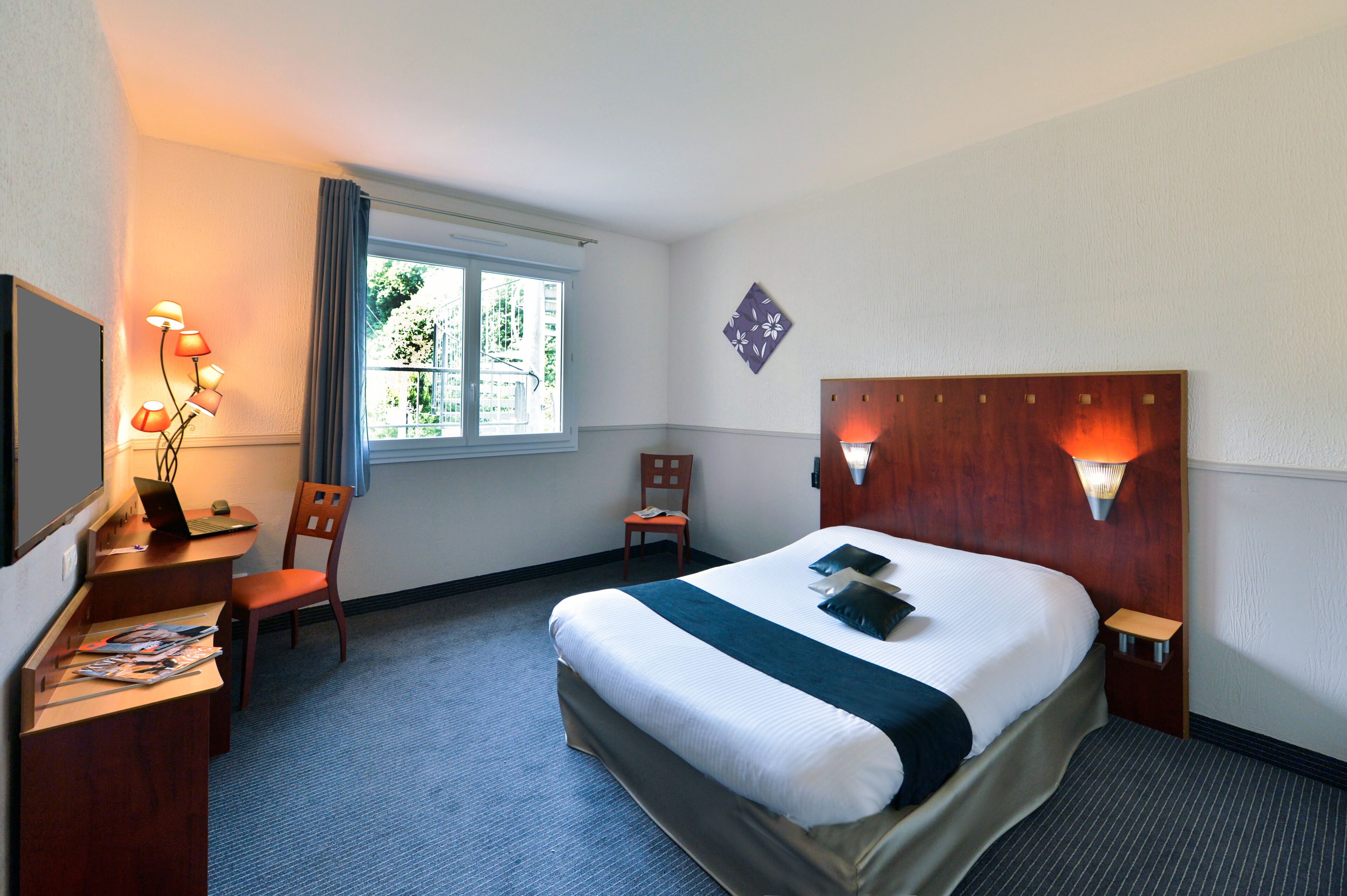 A hotel room with a bed, desk, chair, and a window with curtains.