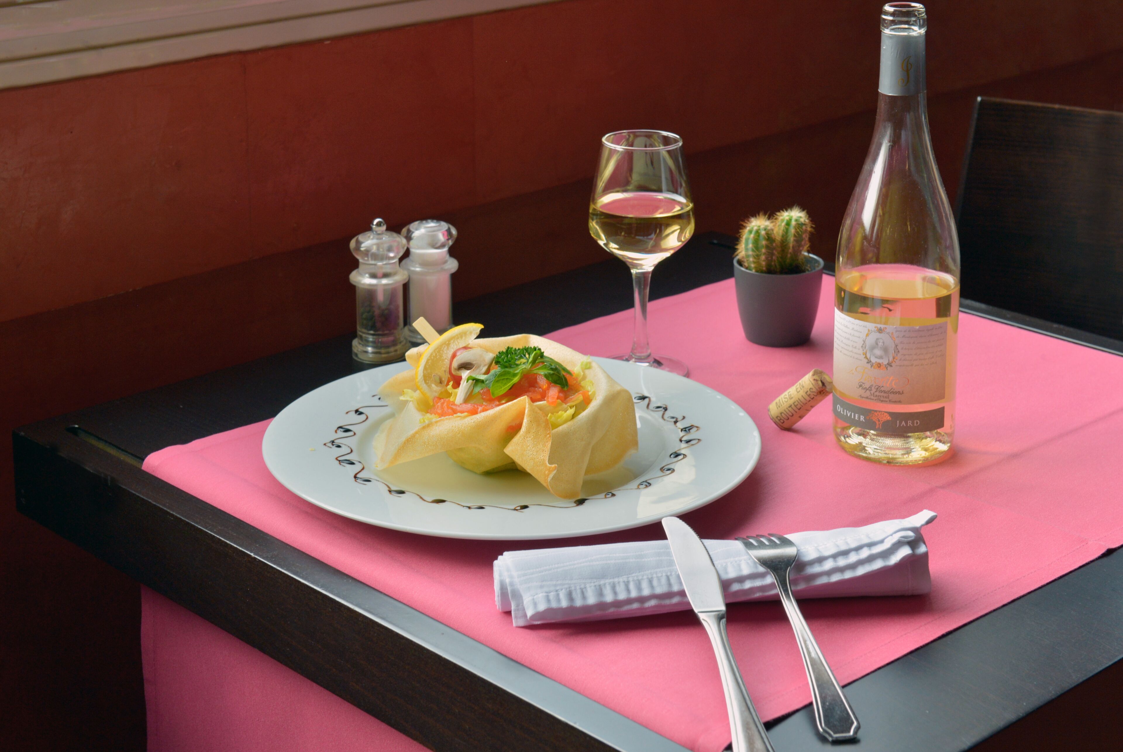 Una mesa de comedor con un plato de comida, una botella de vino, una copa de vino y un juego de tenedor y cuchillo.