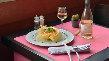 A dining table with a plate of food, a wine bottle, a glass of wine, and a fork and knife set.