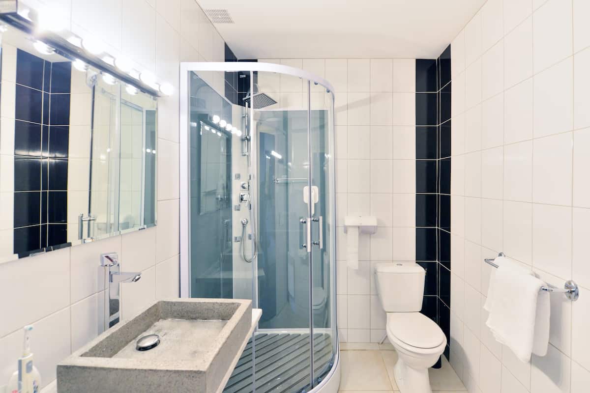 Een moderne badkamer met een douche met glazen wand, een vrijstaand wastafelmeubel, een toilet en een spiegel met verlichting erboven.