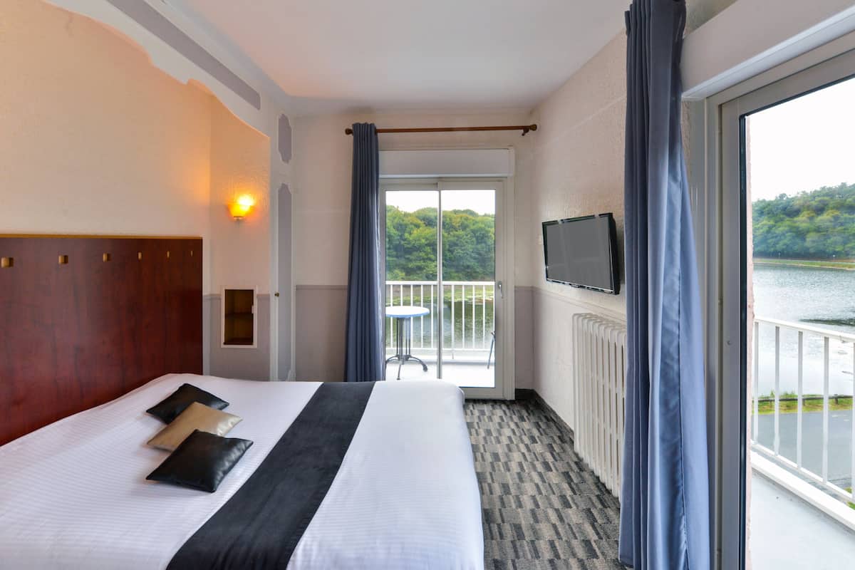 Een hotelkamer met een groot bed, een televisie aan de muur en uitzicht op een meer.