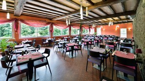 A spacious restaurant with multiple tables and chairs, large windows with red drapes, and hanging pendant lights. - Contact Hôtel le Moulin Neuf (Chantonnay)