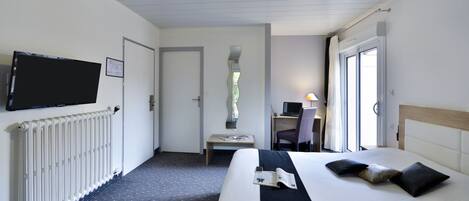 A hotel room with a bed, a desk with a chair, a television mounted on the wall, and a window with curtains.