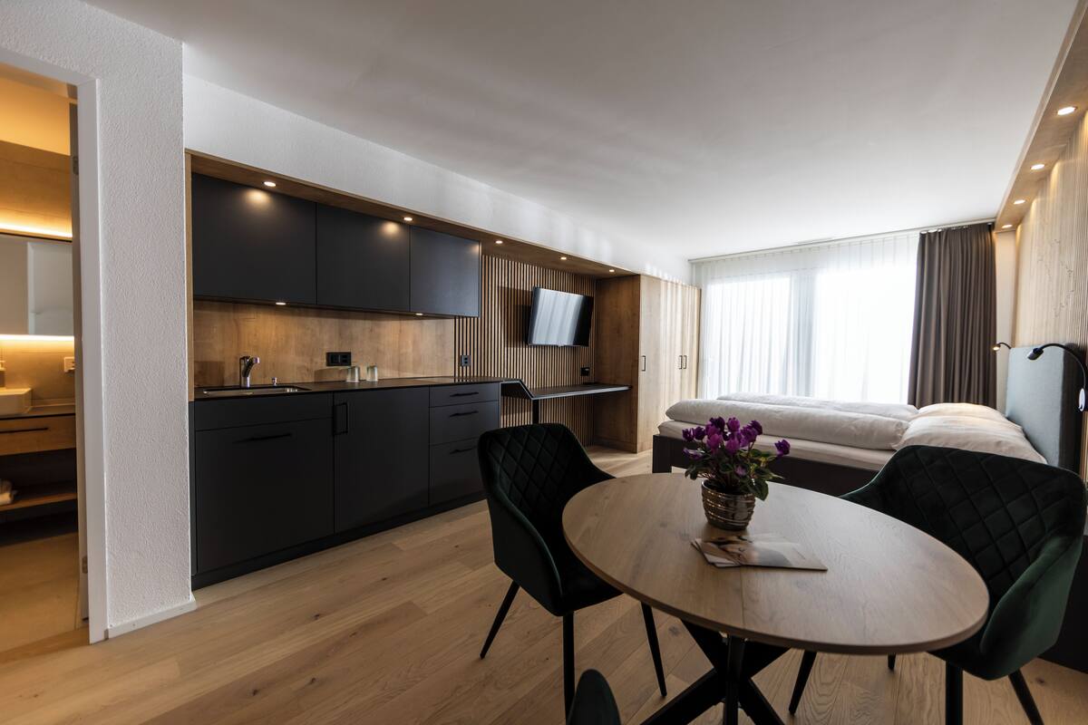 Une chambre d’hôtel moderne dotée d’une kitchenette, d’un coin repas avec une table ronde et d’un canapé-lit.