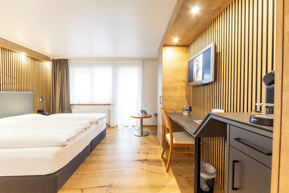 Une chambre d’hôtel équipée d’un lit, d’un bureau, d’une chaise et d’un téléviseur fixé au mur.