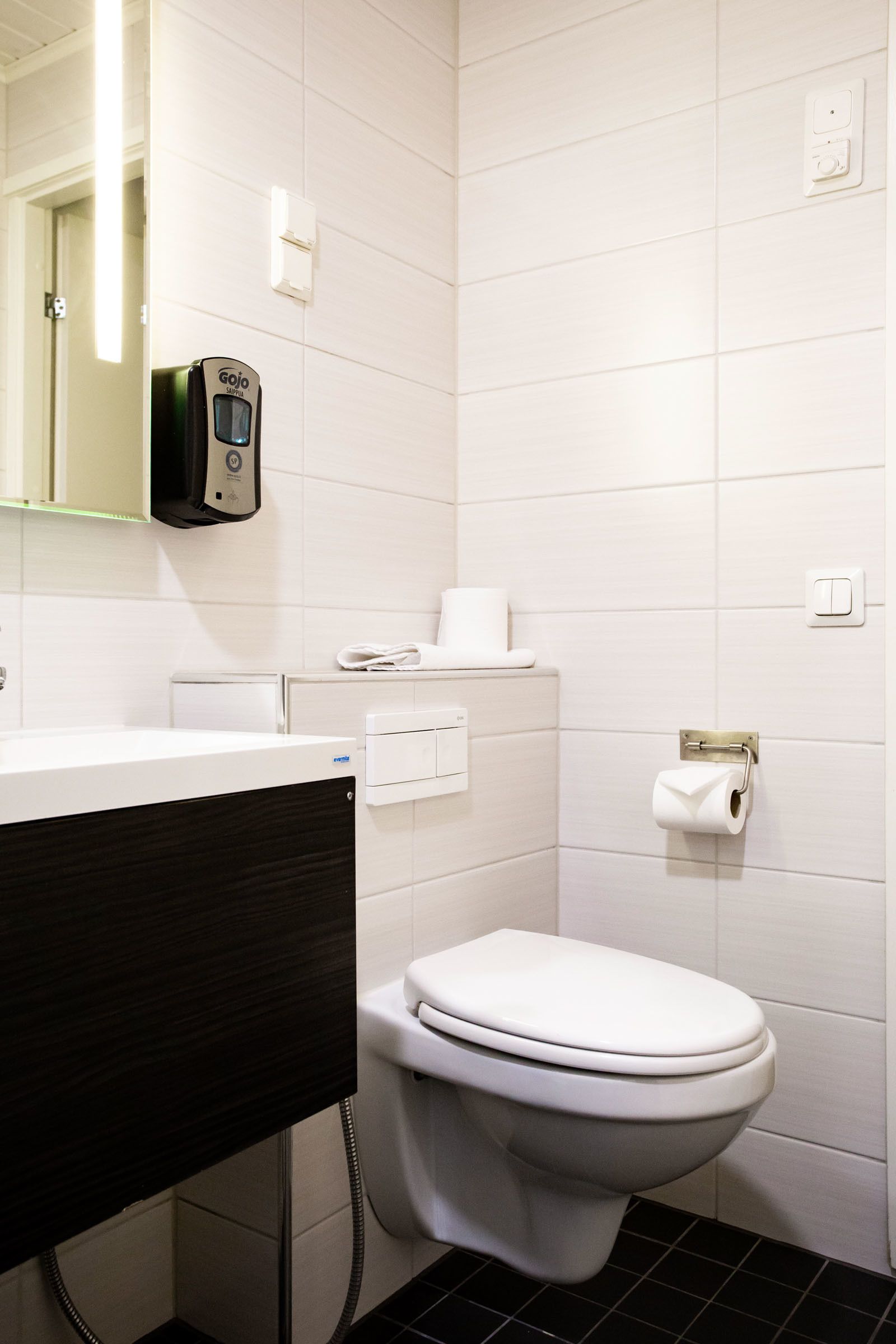 A modern bathroom with a white toilet, a black sink, and a hand dryer.