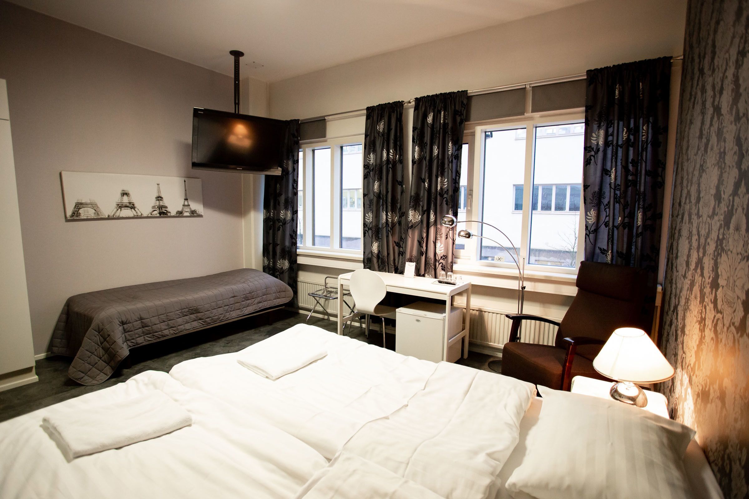 A hotel room with a large bed, a smaller bed, a desk, a chair, and a TV.