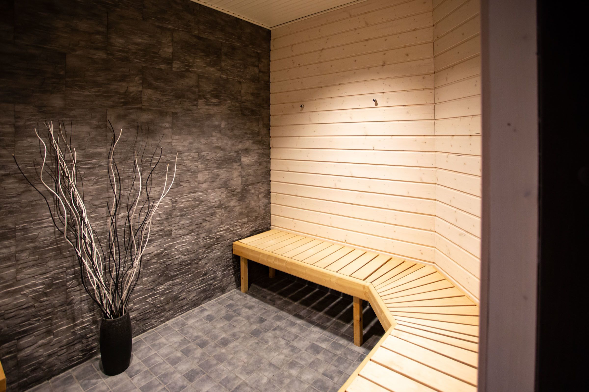 A sauna with a wooden bench, a black vase with branches, and a stone wall.
