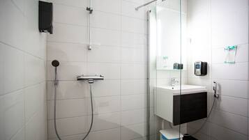 Un baño moderno con ducha de vidrio, lavamanos blanco y mueble negro.