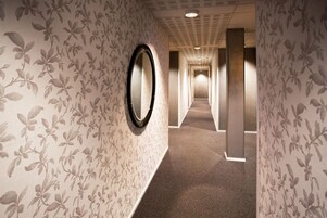 Un pasillo con papel tapiz floral, un espejo redondo y suelo alfombrado.
