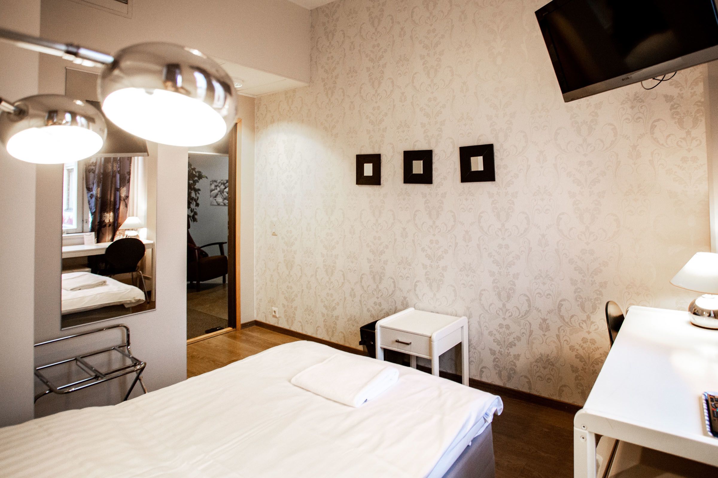 Una habitación de hotel con una cama, un escritorio, una silla, una mesita, un espejo y un televisor montado en la pared.