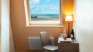 Habitación de hotel con vista a la playa, una silla, una mesa con una botella, vasos y un control remoto.