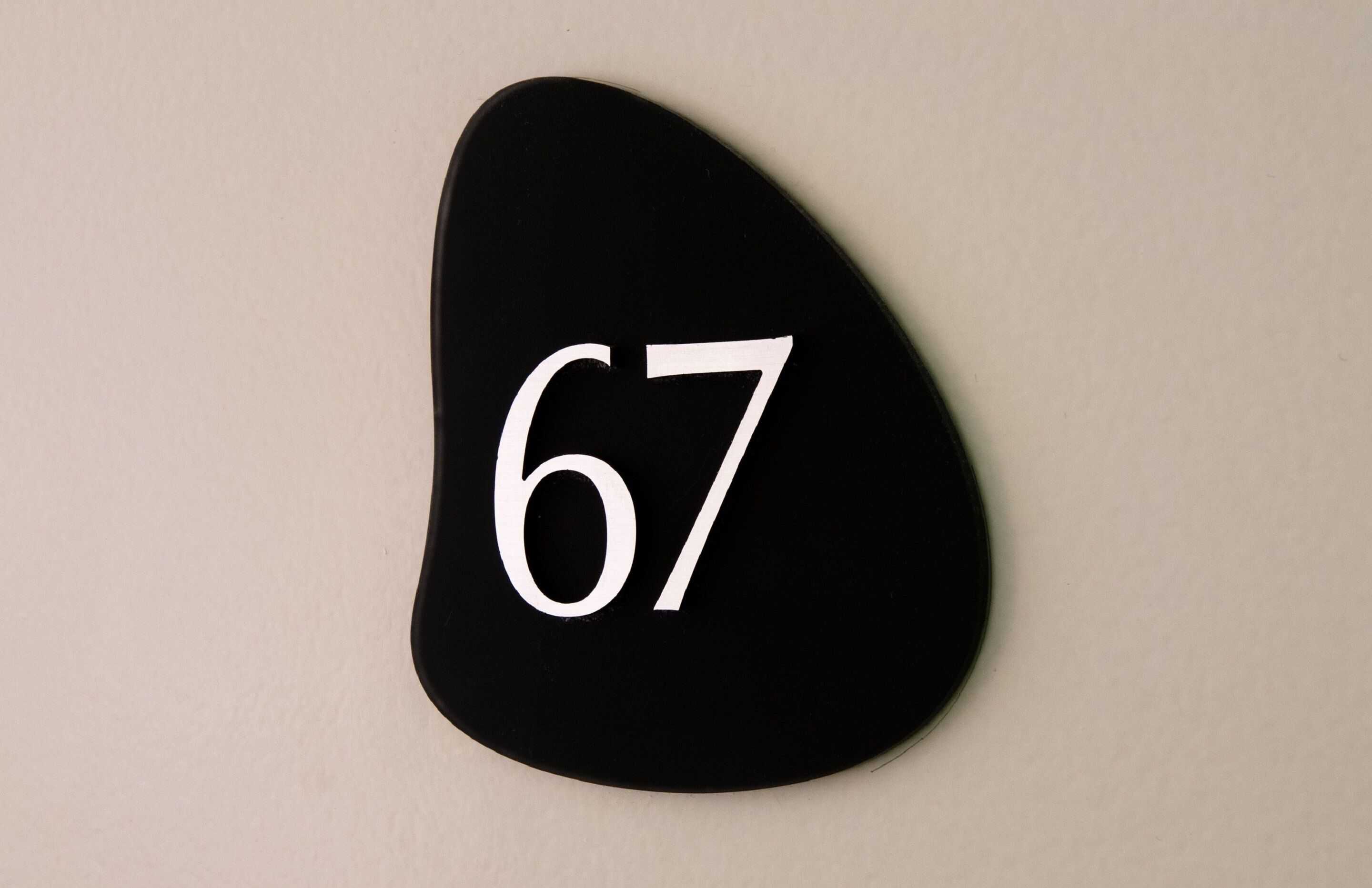 Un panneau noir, de forme ovale, indiquant le numéro de l’immeuble, avec le chiffre 67.