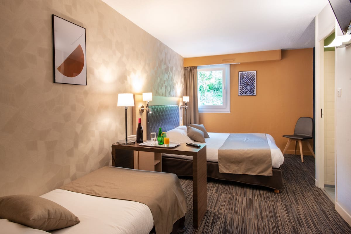 Une chambre d’hôtel avec deux lits, un bureau avec une lampe, une chaise et une fenêtre avec des rideaux.