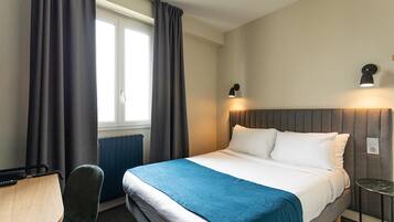 A hotel room with a bed, a desk, a chair, and a window with curtains.