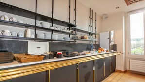 A modern kitchen with black cabinets, a white countertop, and shelves with kitchenware. - Grand Hotel de la Gare (Angers)