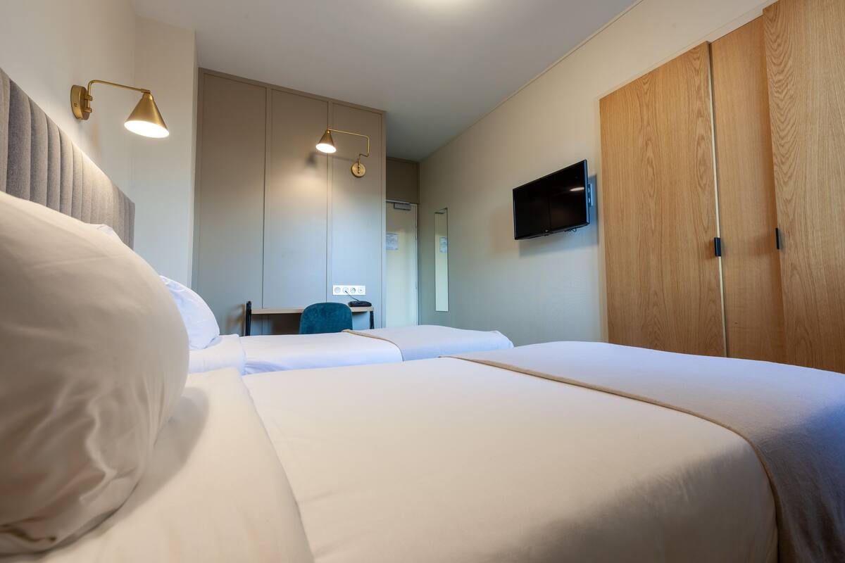 A hotel room with two beds, a desk, a chair, a TV, and a wardrobe.