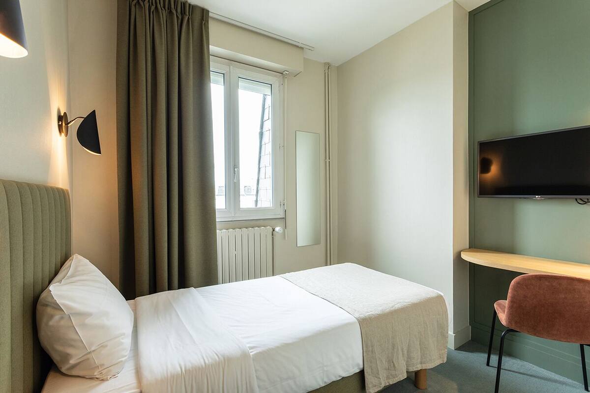 A hotel room with two single beds, a desk, a chair, a TV, and a window with curtains.