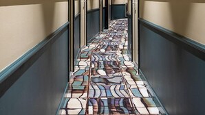 A hallway with patterned floor tiles, doors on both sides, and a ceiling with recessed lighting. - Grand Hotel de la Gare (Angers)