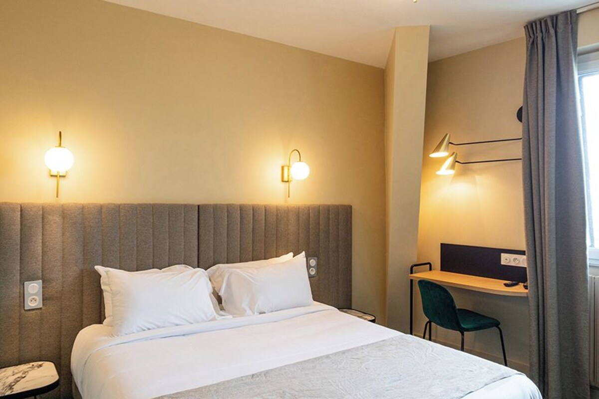 A hotel room with a large bed, two bedside lamps, a desk, and a chair.