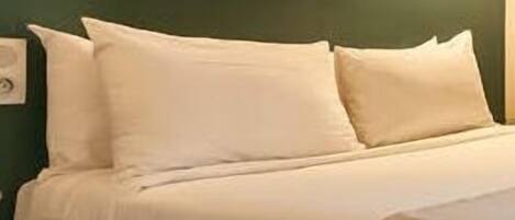 A bed with white bedding, a wooden headboard, and two wall-mounted lamps.