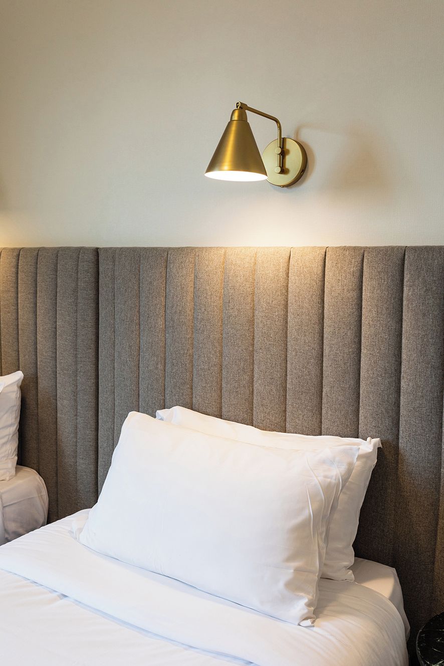 Une chambre d’hôtel avec un lit, une tête de lit et une lampe fixée au mur.