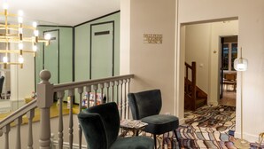 A hotel lobby with a staircase, a black chair, a patterned carpet, and a chandelier. - Grand Hotel de la Gare (Angers)