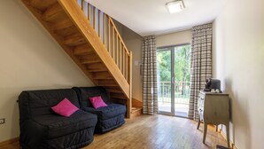 Quarto com escada de madeira, sofá preto com almofadas cor-de-rosa, um banco de madeira e uma pequena mesa com abajur.