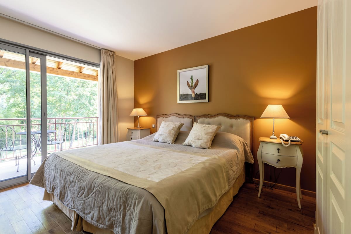Ein Schlafzimmer mit einem großen Bett, zwei Nachttischen mit Lampen, einem gerahmten Bild an der Wand und einem Balkon mit Sitzmöbeln.