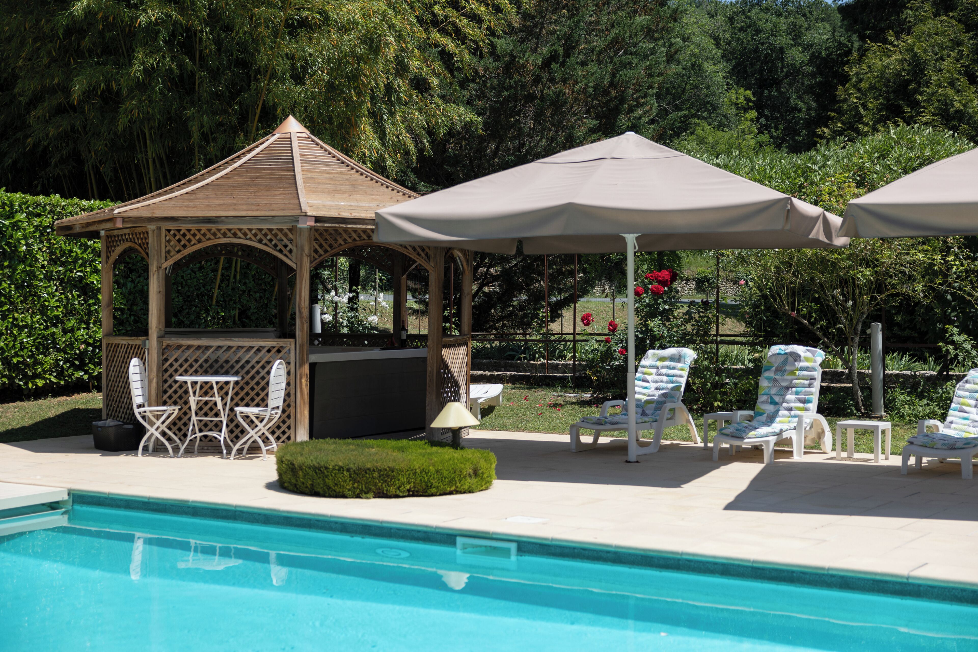 Un área de piscina con un quiosco, sillas de descanso y una mesa con sillas.