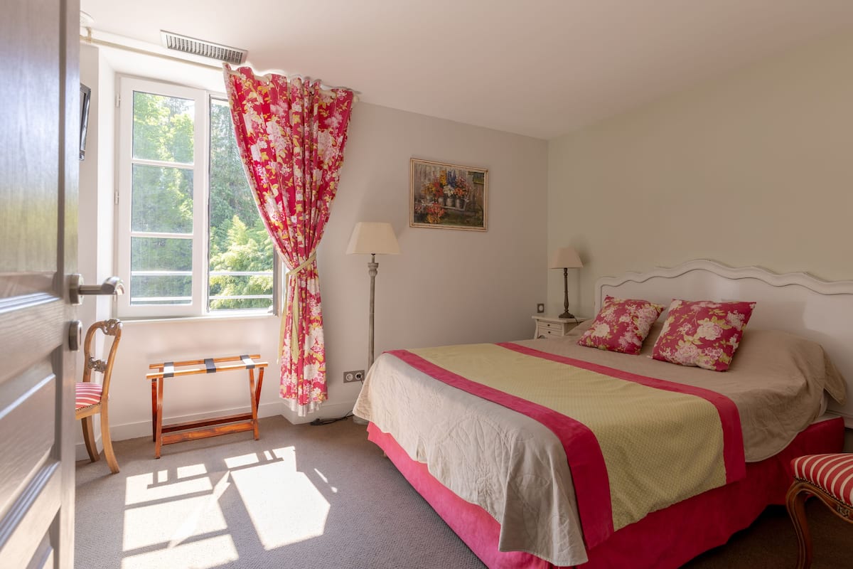 Ein Schlafzimmer mit Bett, Stuhl, Schreibtisch, Fenster und einem Bild an der Wand.