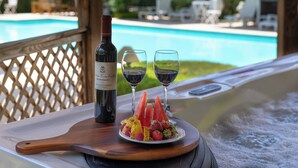 Uma mesa de madeira com uma garrafa de vinho, duas taças e um prato de fruta junto a uma piscina.