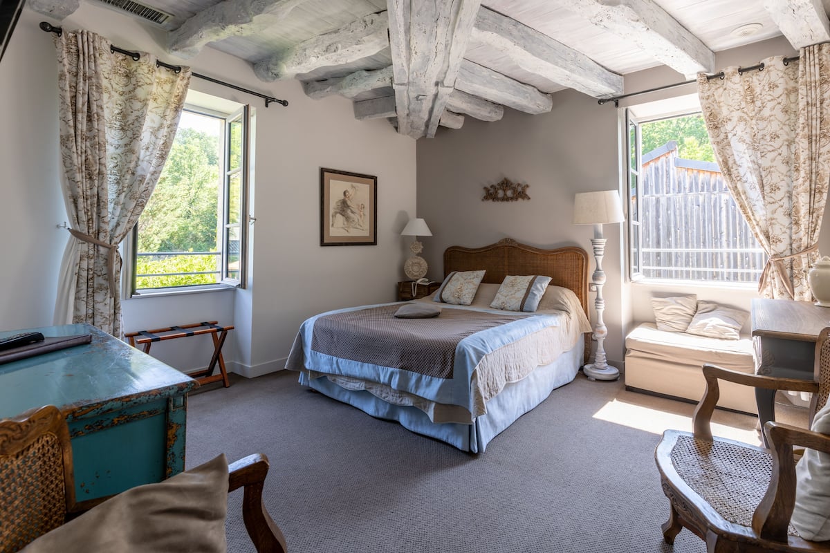 Ein Schlafzimmer mit einem Bett, einem Holztisch, einem Stuhl und einem Fenster mit Vorhängen.