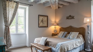 Quarto com cama, mesa de cabeceira, abajur e janela com cortinas.
