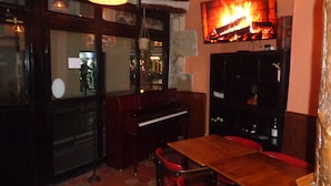 Interior acolhedor de restaurante com mesas e cadeiras de madeira, luminárias de vime suspensas e uma lareira.