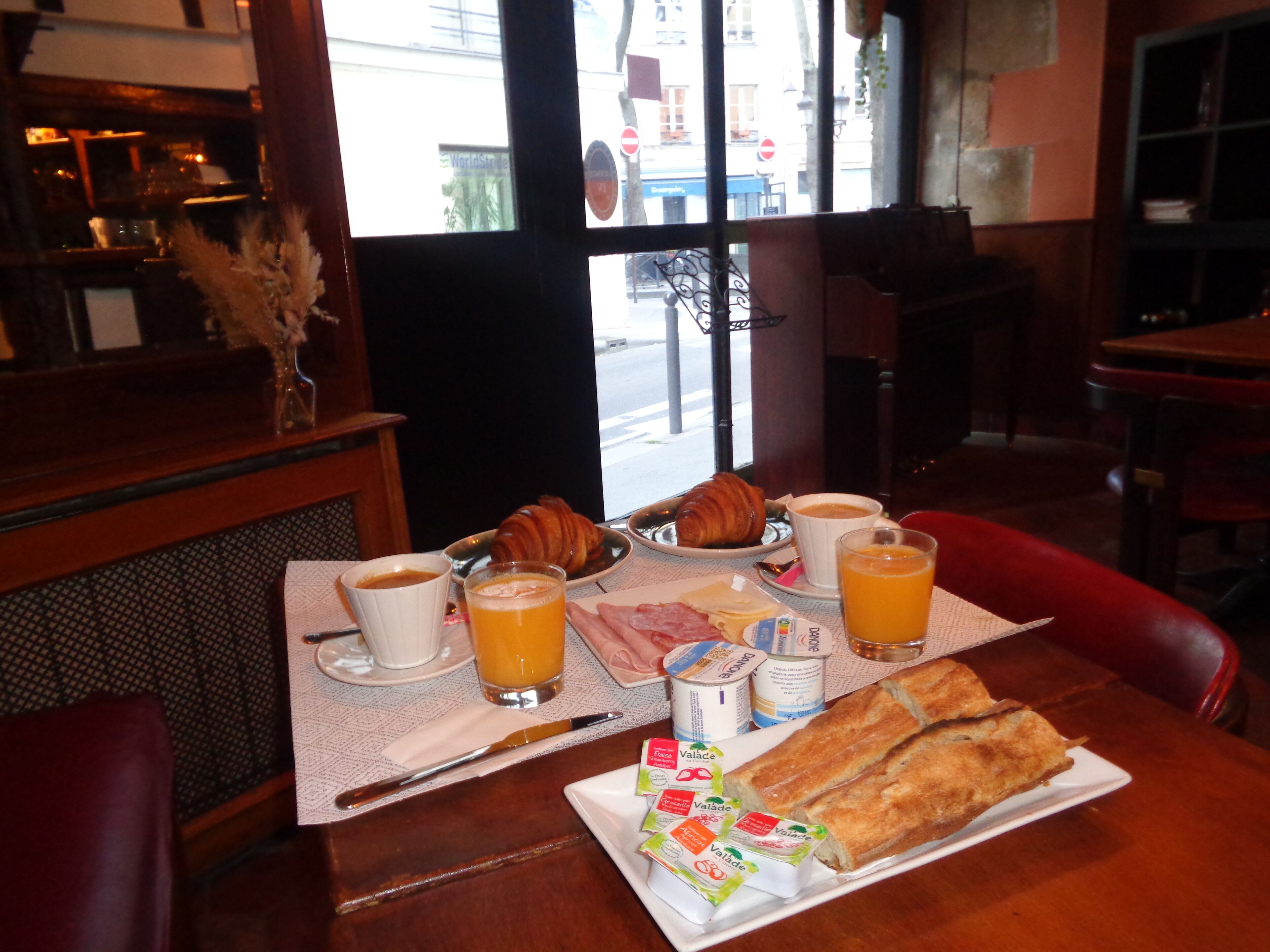 Une table de petit-déjeuner avec des croissants, du café, du jus de fruits et différentes sortes de fromage à tartiner.