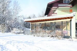 Ein mit Schnee bedecktes Hotel mit einer überdachten Außenbereich-Sitzgelegenheit und einem Schild mit der Aufschrift 'Thermenhotel Stöbinger Hof'.