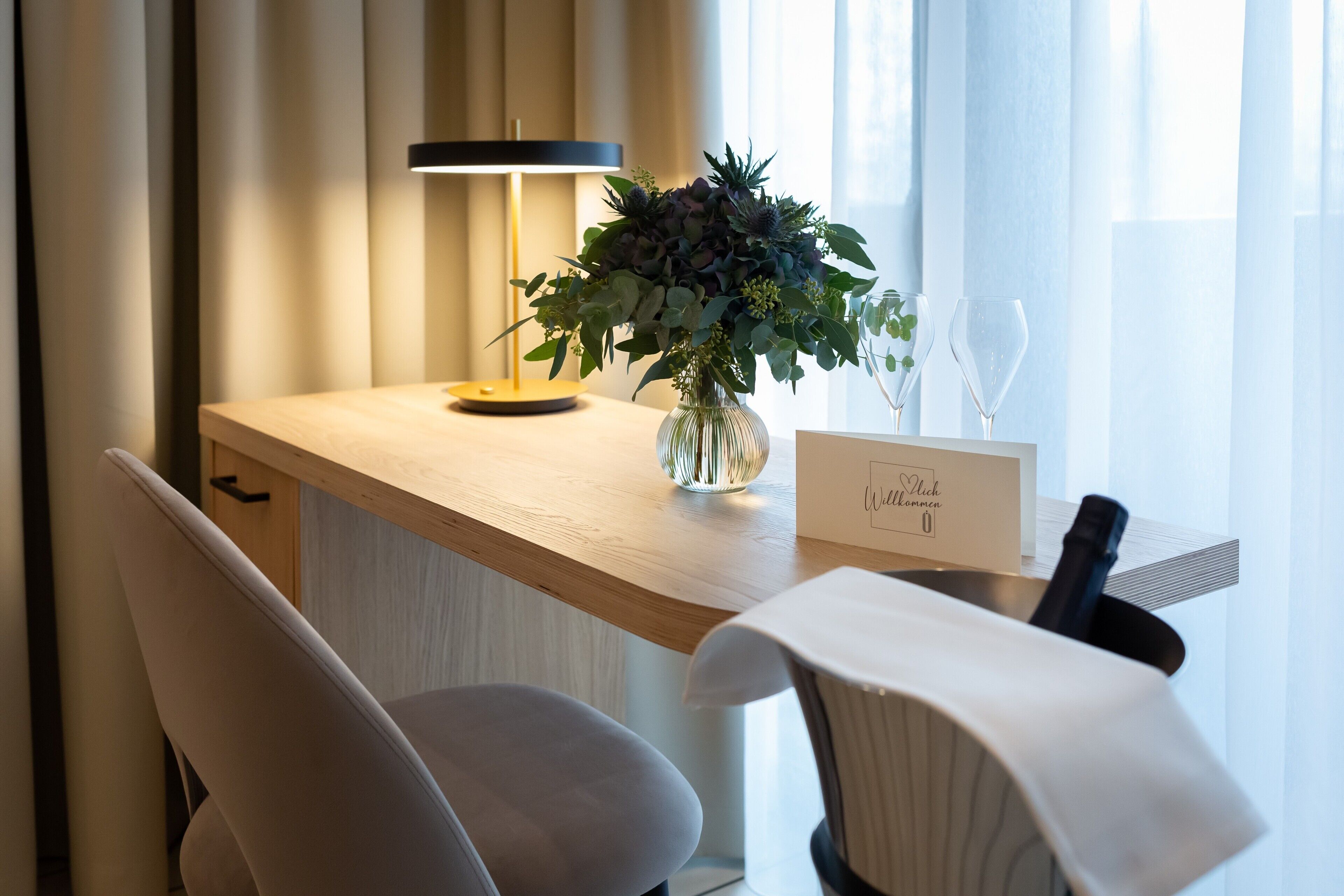 Una habitación de hotel moderna con un escritorio de madera, un florero, una copa de vino y un cartel con un símbolo de corazón.