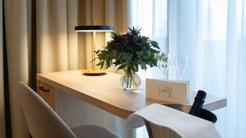 Una habitación de hotel moderna con un escritorio de madera, un florero, una copa de vino y un cartel con un símbolo de corazón.