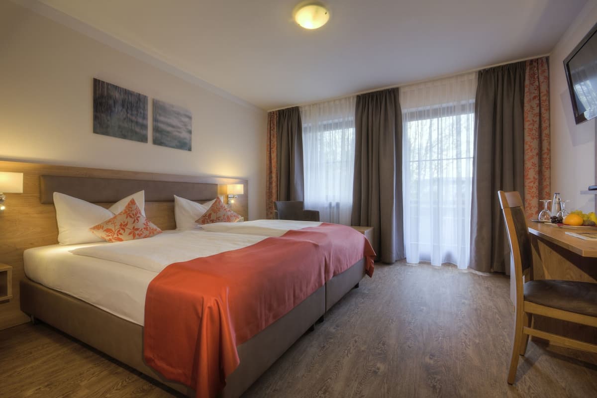 A hotel room with a large bed, a desk with a chair, and a television on the wall.