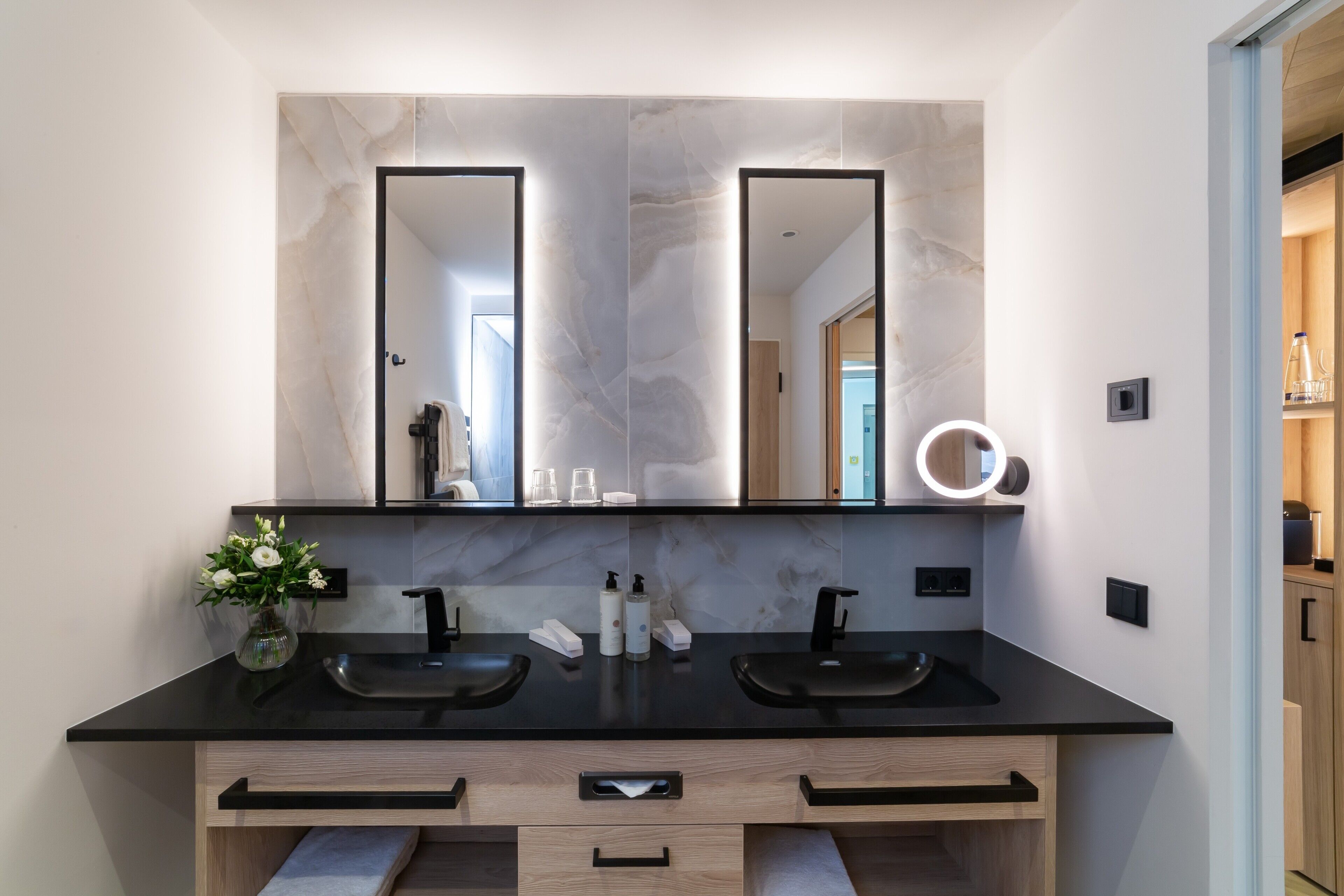 A modern bathroom with two sinks, a large mirror, and a vase of flowers.