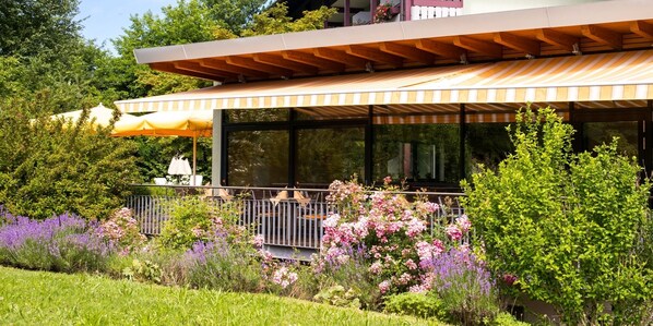 Una casa moderna con patio cubierto, jardín exuberante y grandes ventanales.