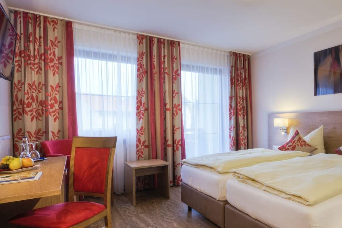 A hotel room with a bed, a desk with a chair, a small table with a chair, and a painting on the wall.