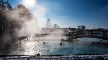 A hot spring with a wooden bridge, steam rising from the water, and a clear sky.