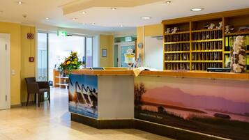 A reception area with a desk, chairs, a flower arrangement, a bookshelf, and a mural.