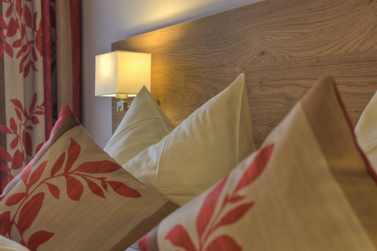 A hotel room with a wooden headboard, a bedside lamp, and pillows with a red leaf pattern.