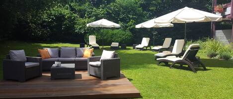 An outdoor patio with wicker furniture, including a sofa and chairs, and two large umbrellas.