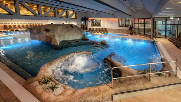 An indoor swimming pool with a rock formation and a hot tub area.