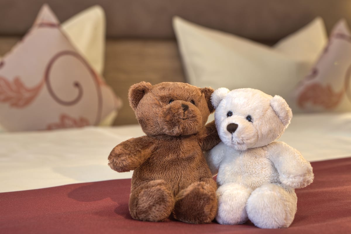Two teddy bears on a bed with pillows in the background.